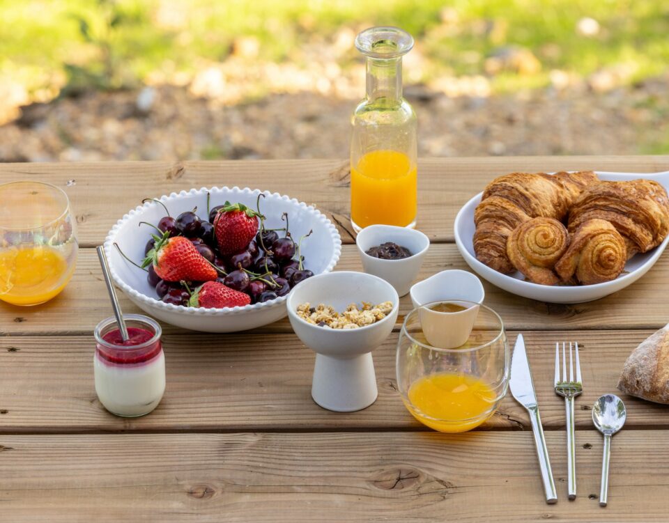 Petit-déjeuner gourmand en terrasse : viennoiseries, fruits frais, granola et jus d'orange – Les Safranières, Sauveterre-de-Rouergue